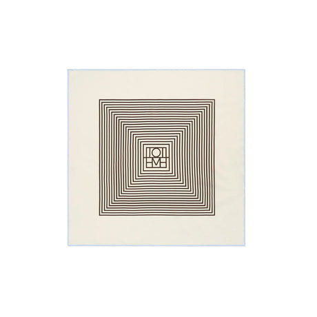 An off-white square fabric item, likely a bandana or napkin, featuring a central geometric design of concentric dark brown squares and a central monogram logo.